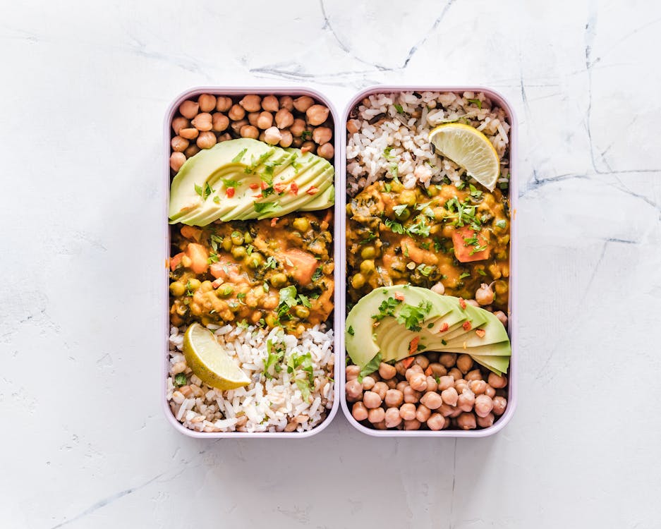 Free Delicious vegan lunchboxes featuring chickpeas, rice, avocado, and curry on a white background. Stock Photo