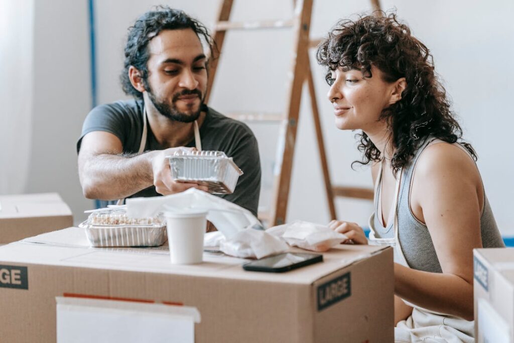 Free A couple relaxes with takeout food amidst moving boxes in their new home. Stock Photo